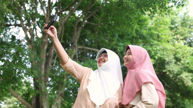 Cheerfulness family two muslim mothers and daughters walked in a shady garden, delighted that the daughters showed her photos from a smartphone camera talked good mood strengthened family relation.