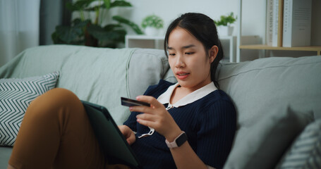 Selective focus of Asian teenager woman sitting on sofa holding credit card making online payment...