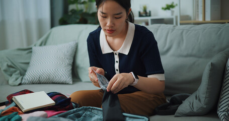 Front view of Asian teenager woman sitting on sofa packing travel luggage with personal items for traveling trip, Preparation travel suitcase at home. - 772699472