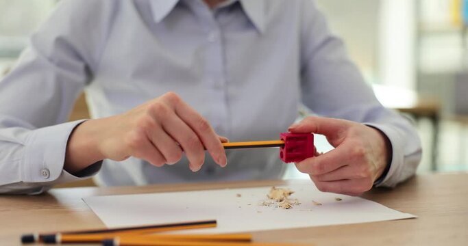 Closeup of woman hands sharpening a pencil with red sharpener at workplace