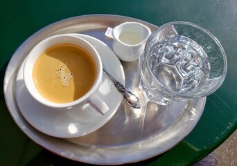A cup of coffee, a creamer and ice water, served on a silver platter.