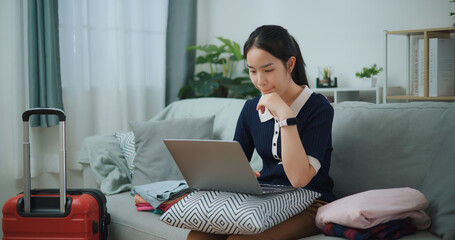 Portrait of Asian teenager woman sitting on sofa using laptop for prepare booking hotel and airplane ticket for travel. backpacker travel concept. - 772699650