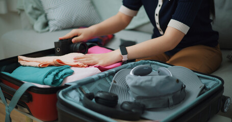 Selective focus hands of Asian teenager woman sitting on sofa packing travel luggage with clothes for traveling trip, Preparation travel suitcase at home. - 772700044
