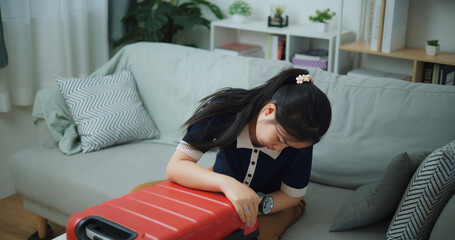 High angle view of Asian teenager woman sitting on sofa is closing a packed suitcase in the living...