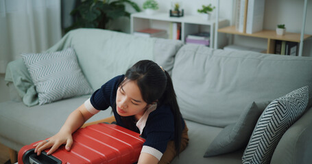 High angle view of Asian teenager woman sitting on sofa is closing a packed suitcase in the living room, Preparation travel suitcase at home. - 772700201