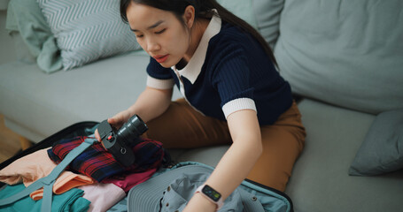 High angle view of Asian teenager woman sitting on sofa packing travel luggage with personal items for traveling trip, Preparation travel suitcase at home. - 772700202