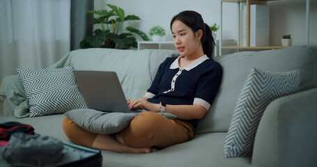 Portrait of Asian teenager woman sitting on sofa using laptop for prepare booking hotel and airplane ticket for travel. backpacker travel concept. - 772700219