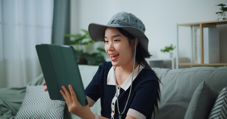 Selective focus of Asian teenager woman sitting on sofa video call with friend while packing suitcase luggage for travelling, backpacker travel concept. - 772700401