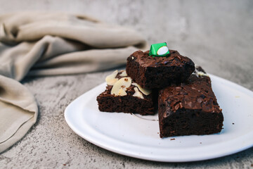 Homemade brownies with almond slices and choco bar on top, served on white plate. 