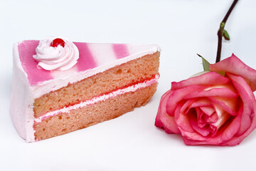 Slice of pink cake with white cream red jelly on the top and pink rose on white plate background
