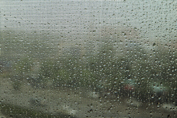 Image of water droplets on clear glass looking through the black screen in rainy season. Image use for meteorology forecast and graphic background.