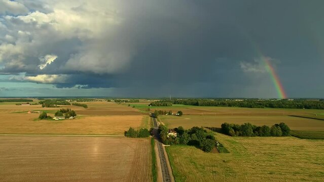 Aerial view of cloudburst in countryside of Latvia, agricultural meadow covered in sunshine.