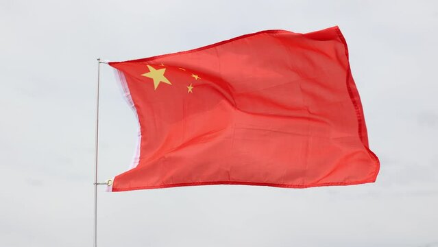 National flag of China with five golden-yellow stars shining on red silk symbolizing revolution, vitality and unity of Chinese people and Communist Party fluttering on flagstaff against cloudy sky 