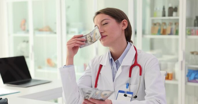 Enthusiastic female doctor sniffs money earned by medical practice