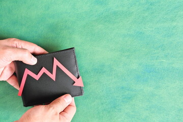 Male hand holding a wallet with red downward arrow. Money value currency depreciation and inflation...