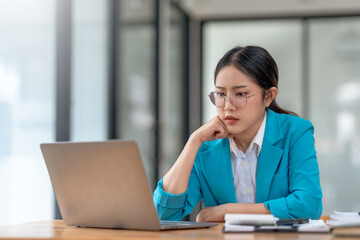 Fototapeta premium Stressed asian businesswoman working at laptop in office. Work pressure and deadline concept.