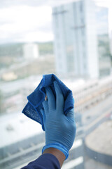 hand in blue glove cleaning window with green rag