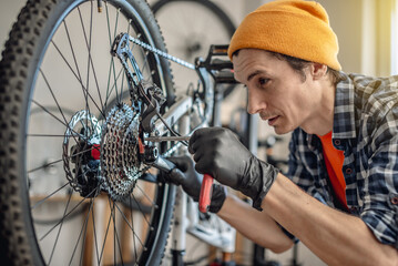 A male bicycle mechanic in the workshop disassembles a mountain bike and repairs it. Maintenance concept, preparation for the new season - 772737650