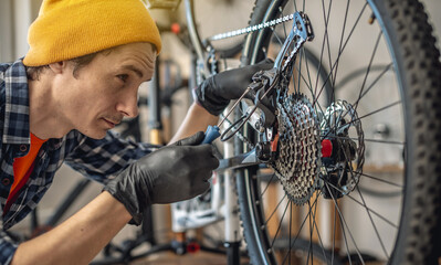 A male bicycle mechanic in the workshop disassembles a mountain bike and repairs it. Maintenance...