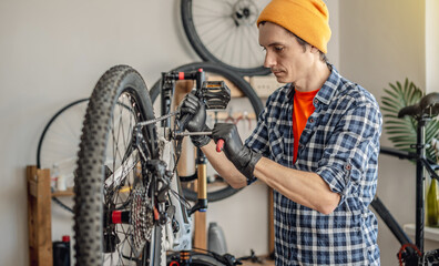A male bicycle mechanic repairs a mountain bike in a workshop. The concept of preparation for the new season, repair and maintenance - obrazy, fototapety, plakaty