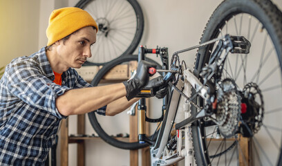 A male bicycle mechanic repairs a mountain bike in a workshop. The concept of preparation for the new season, repair and maintenance - 772738211
