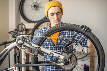 A male bicycle mechanic in the workshop disassembles a mountain bike and repairs it. Maintenance concept, preparation for the new season - 772738639