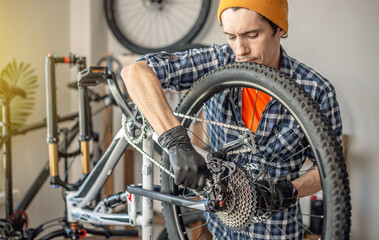 A male bicycle mechanic in the workshop disassembles a mountain bike and repairs it. Maintenance concept, preparation for the new season