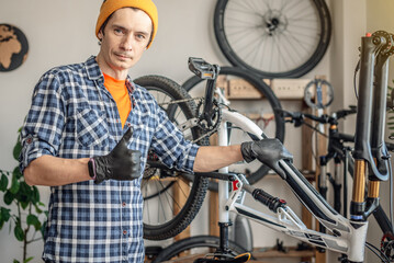 A male bicycle mechanic in the workshop disassembles a mountain bike and repairs it. Maintenance concept, preparation for the new season - 772739469