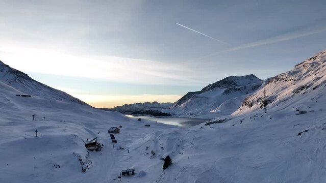 Dawn on gorgeous snow mountains with frozen lake and refuge house, Mont Cenis
