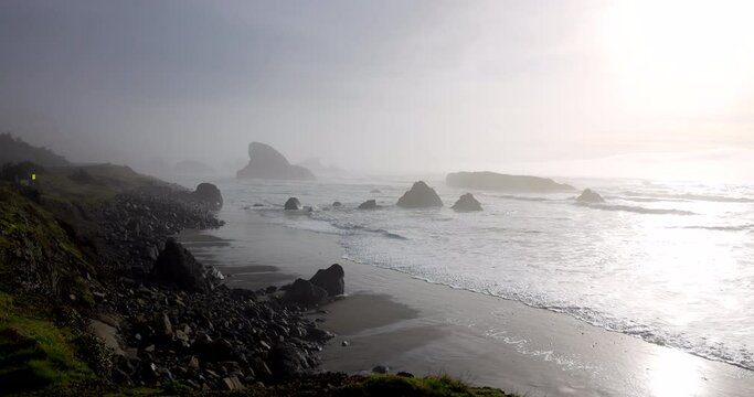 A foggy beach with a rocky shoreline. The water is calm and the sky is overcast