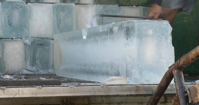 close up of the worker is using a metal hook to cut a block of ice from the middle