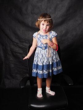 little girl in a blue dress and jewelry on a black background in the studio in full growth
