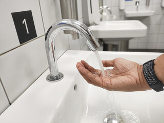 Closeup image of a man washes his hands using a touchless faucet.