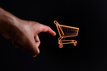 Hand pointing at glowing shopping cart on black background. Online shopping concept.