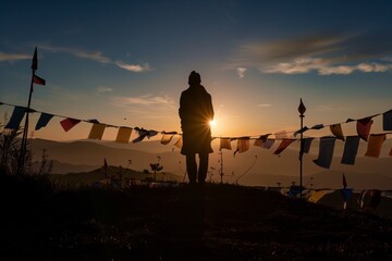 silhouette of person at sunrise surrounded by prayer flags on hilltop