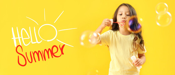 Fototapeta premium Cute little girl blowing soap bubbles on yellow background