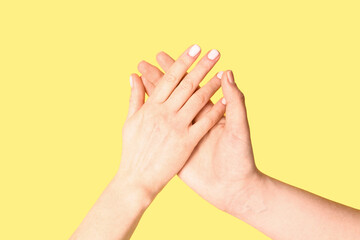 Women holding hands together on yellow background. Friendship concept