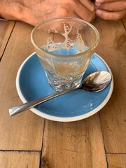 An empty cup of cortado coffee on a wooden table with a man’s hands in the background