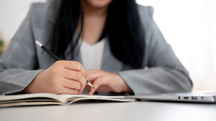 A cropped shot of a businesswoman focused on writing or taking notes in the notebook with a pencil.