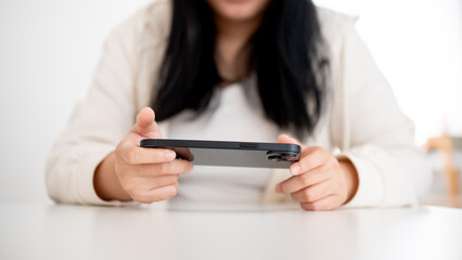 A young Asian woman is using her smartphone, watching a video or playing a mobile game indoors.