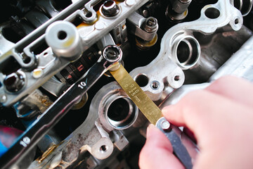 Car mechanic checking and adjusting valves of car engine with feeler gauge or thickness gauge tool,...