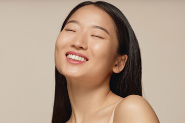 Closeup studio portrait of happy young Asian woman with long straight hair smiling with eyes closed