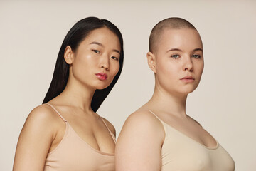 Studio portrait of self-confident young Asian and Caucasian women wearing neutral toned bras posing...