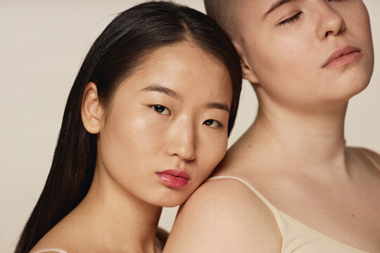Conceptual studio portrait of diverse young Asian and Caucasian women wearing neutral toned underwear posing for camera
