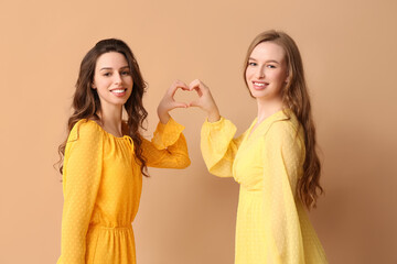 Happy smiling young sisters making heart with hands on beige background