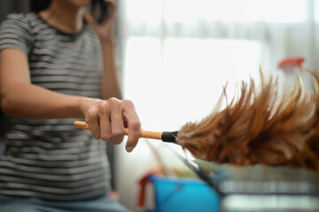 Closeup young woman woman dusting shelf, cleaning her house. Chores and hygiene concept