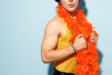 Side view cropped close up young happy gay Latin man wearing mesh tank top hat yellow clothes tinsel garland isolated on plain blue background studio portrait. Pride day June month love LGBT concept.