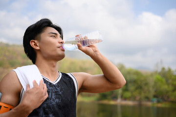 Handsome athlete man drinking water from a bottle taking a break from workout in the park
