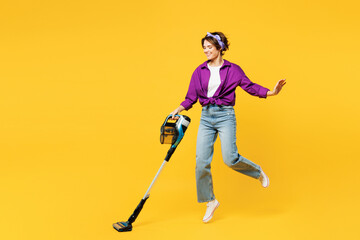 Full body side view happy fun young woman wear purple shirt casual clothes do housework tidy up hold vacuum cleaner jump high isolated on plain yellow background studio portrait. Housekeeping concept.