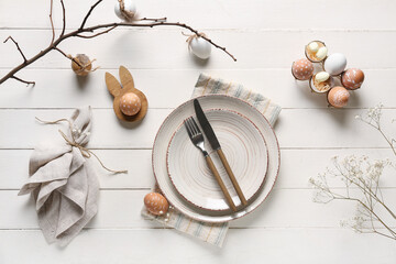 Table setting for Easter celebration with branch and painted eggs on white wooden background. Top...